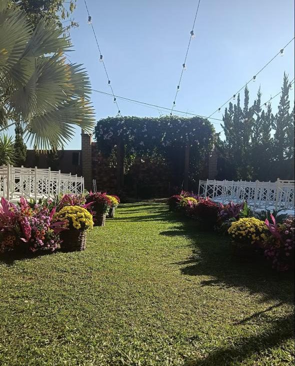 Corredor de grama com arranjos de flores coloridas levando ao pergolado florido