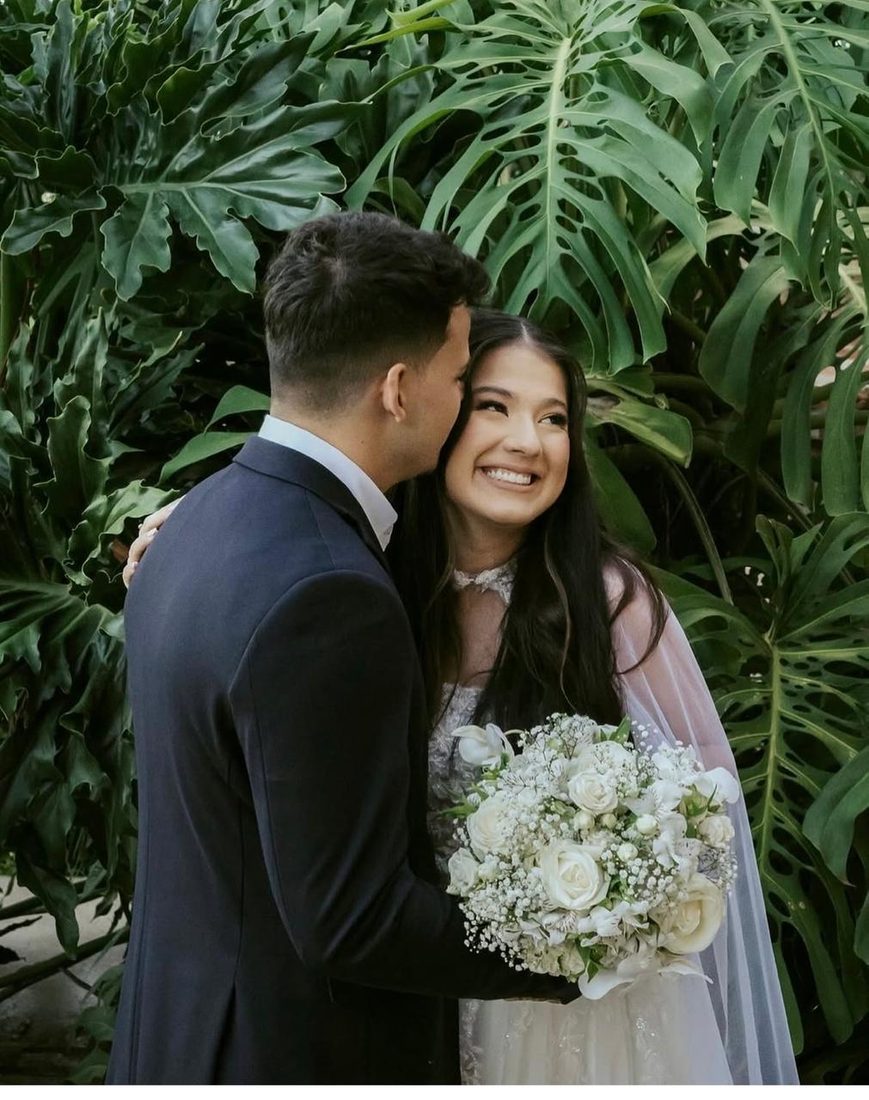 Noiva sorrindo abraçada ao noivo diante das folhagens do jardim
